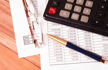 Pen, glasses and calculator on paper tables with numbers