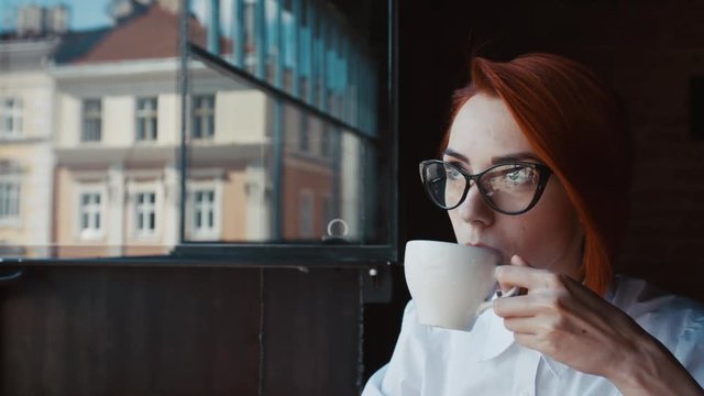 Young beautiful happy smiling woman drinking tea or coffee and looking through the window. Close up
