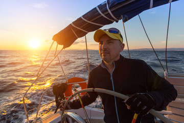 Captain steers the sailing yacht on the sea during sunset.