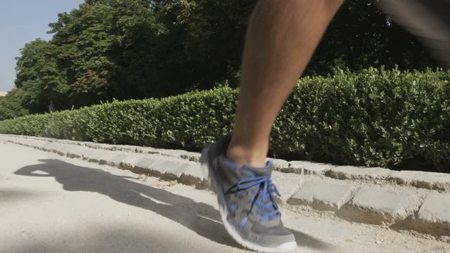 Running man sprinting fast at speed with close up of running shoes. Male sprinter in city park, El Retiro Madrid, Spain. RED EPIC SLOW MOTION.
