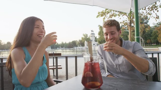 Couple drinking sangria toasting happy having fun sitting at cafe table outdoors in Madrid, Spain in El Retiro city park. Romantic couple lifestyle in Buen Retiro Park, Parque el Retiro.