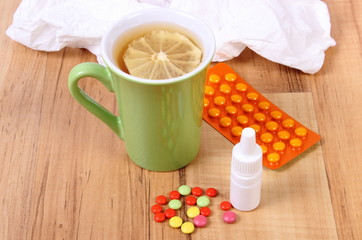 Pills and nose drops for colds, handkerchiefs and hot tea with lemon