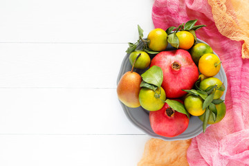 A beautiful set of fruits pomegranate, tangerine, pear on pink textile and white wooden background horizontal image