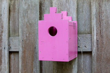 Pink birdhouse on a wooden fence
