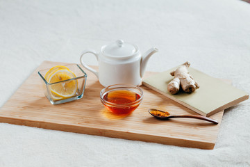 Obraz na płótnie Canvas Herbal tea with chamomile flowers, turmeric and honey on a wooden board. Treatment of hot drink with ginger. Treatment of folk remedies in bed.