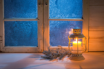 Frosted blue window with burning candle for Christmas at night