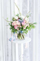 a cute bouquet of massive pink flowers with green brunches standing on a high white stand, lace white curtains behind