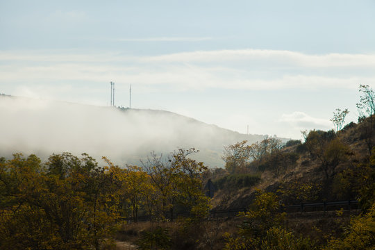 Fototapeta Montaña con niebla / Montaña cubierta de niebla con dos antenas de telefonía en la cima
