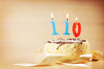 Birthday cake with burning candle as a number one hundred and ten. Focus on the candle
