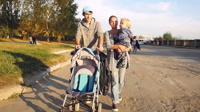Young happy family with a little son walking together in autumn promenade during sunset in slowmotion