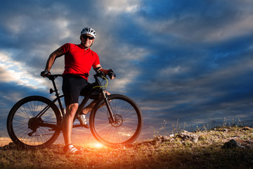 Naklejka na ściany i meble Cyclist riding mountain bike on trail at evening.