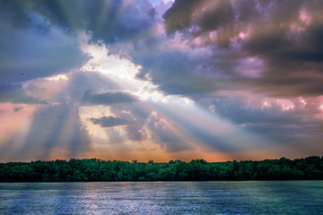 Naklejka na ściany i meble Sun rays light through down from rain clouds and reflected in water
