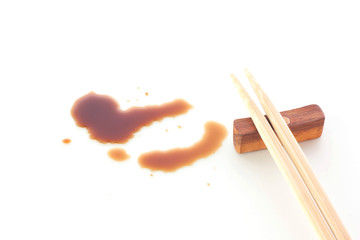 Splashes of soy sauce and chopsticks on white background.
