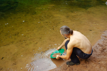 man, prospector panning gold in a river with sluice box