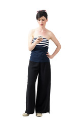 Frustrated young trendy woman in wide-leg pants typing message on cellphone. Full body length portrait isolated over white studio background.