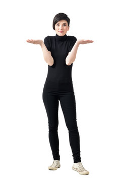 Funny confused clueless young woman in black turtleneck and pants shrugging shoulders. Full body length portrait isolated over white studio background.