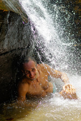 Man taking a relaxing shower under waterfall. outside