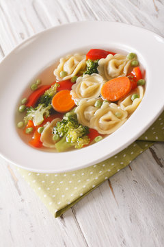 tortellini soup with broccoli, peas, carrot and pepper close-up. vertical
