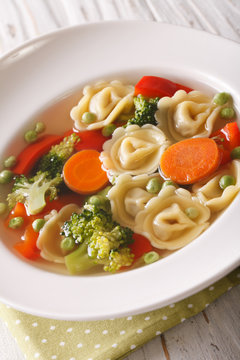 Italian soup with tortellini and vegetables closeup at the plate. Vertical
