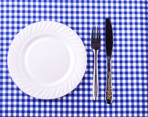 Empy plate and with a knife fork on the tablecloth in a cage