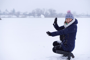 young adult girl women sit on a ground hands arms at her frown face covering defending from the throwed snowball which flight right at her head.