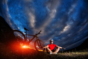 Man cyclist is engaged in yoga on a sunset - obrazy, fototapety, plakaty