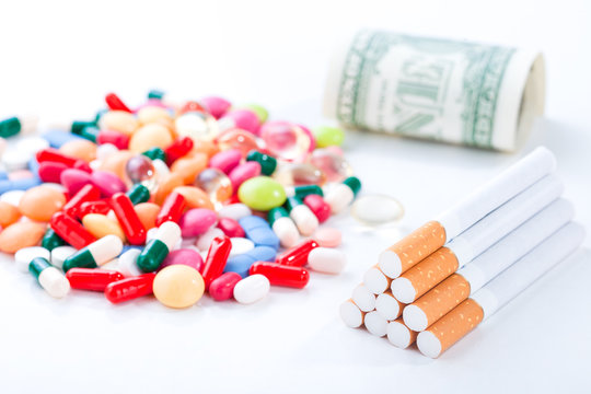 Cigarettes, colorful pills and tablets with dollar bill on a white background