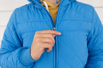 man buttons blue quilted jacket. cropped image of a man's hand fastens with a zipper on the jacket on a white background. close up