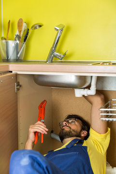 plumber repairing water faucet under kitchen sink