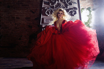 Fashion photo of young magnificent woman. Running towards camera. Seductive blonde in red dress with fluffy skirt