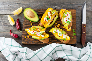 Bruschetta with avocado, yellow pepper, grains of corn, parsley and chili peppers on old wooden background. Selective focus.