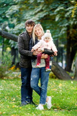 Fototapeta premium Cheerful parents with child standing in autumn park