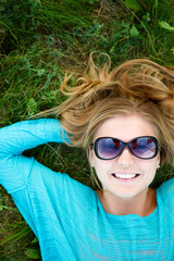 Fototapeta premium Cheerful beautiful girl lying on grass with hands behind head