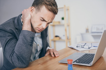 Sad young man having pain in the neck