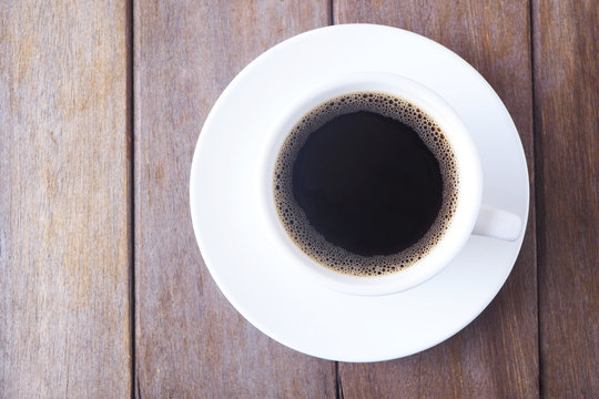 Top view of a cup of black coffee on a wooden table.