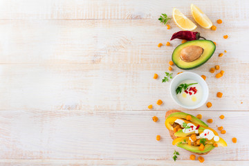 Bruschetta with avocado, yellow pepper, grains of corn, parsley and chili pepper on a light wooden background. Selective focus.