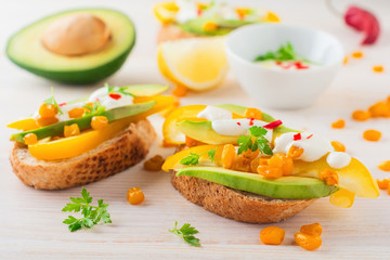 Bruschetta with avocado, yellow pepper, grains of corn, parsley and chili pepper on a light wooden background. Selective focus.
