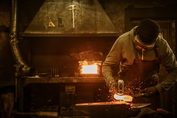 Blacksmith with brush handles the molten metal on the anvil in smithy