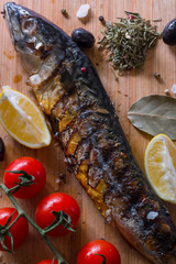 Mackerel fish on a wooden board with tomatoes and herbs