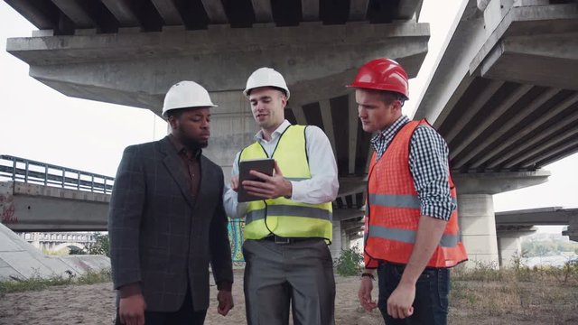 4K shot of three multiracial young male architects having a discussion on site about a building design standing in a row facing the camera, three-quarter closeup view