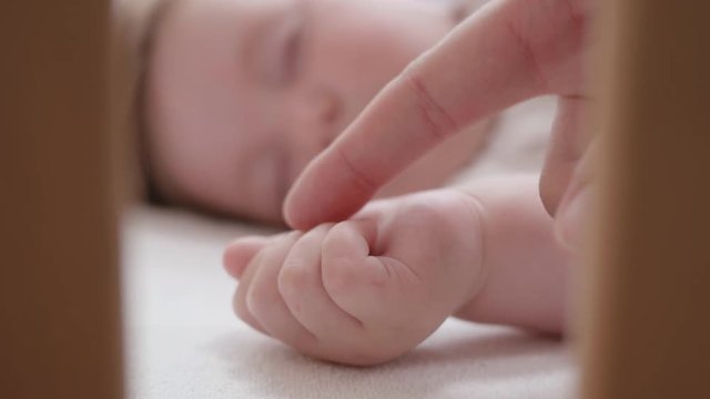 Handheld shot - mother caressing sleeping baby's hand. 
