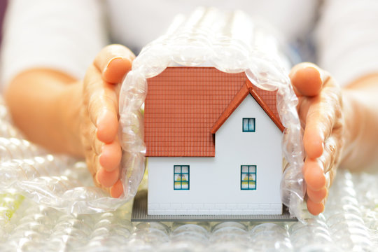 Woman hands covering a model house with bubble wrap- house protection or insurance concept