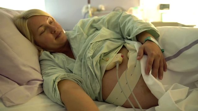 A pregnant woman is lying on the bed and she is waiting to give birth soon. Close-up shot.
