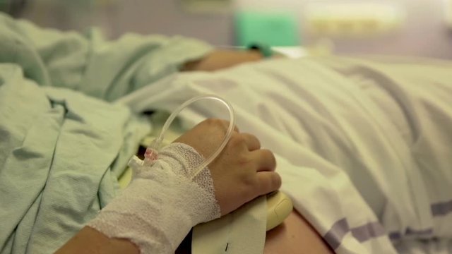 A pregnant woman is resting on a hospital bed and she has an injection in her hand. Close-up shot.
