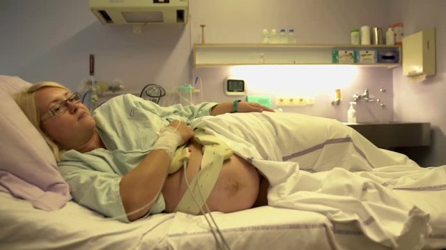 A pregnant woman is resting on the hospital bed and she is about to give birth anytime soon . She is lying on her hip. Wide-angle shot.
