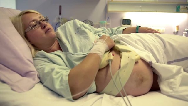 A pregnant woman is lying on the hip on the hospital bed. She is resting and is ready to give birth anytime soon. Wide-angle shot.
