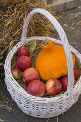white wicker basket with red apples and orange pumpkin near haystack