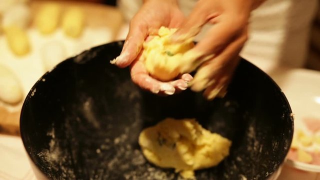 Mani di una donna che Impastano crocchette di patate ripiene in una grande ciotola nera. 