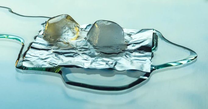 Two ice cubes melting on the glass surface on a background of running clouds. Time lapse