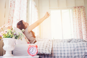 young woman wake up stretch on the bed in the morning alarm cloc